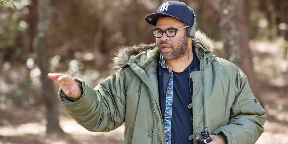 Jordan Peele bundled up in a coat, and pointing at something off-camera