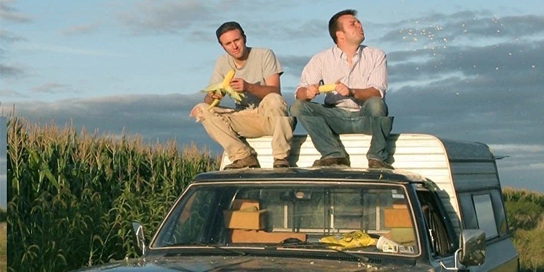 Two friends sit on a truck by a cornfield