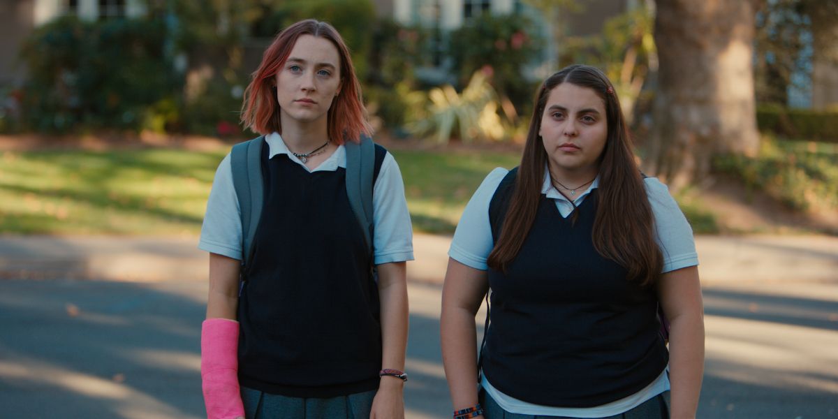 Lady Bird wearing pink cast and school uniform standing next to Julie in Lady Bird