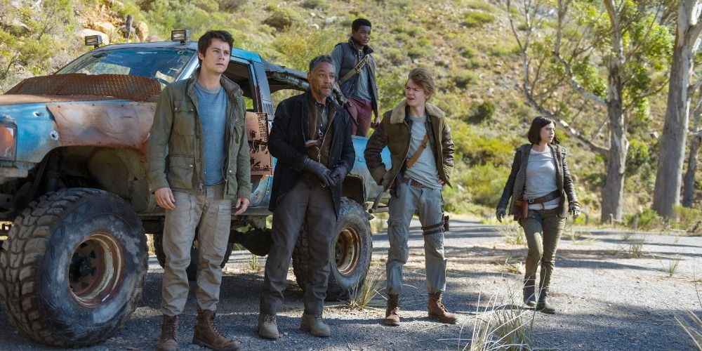 Thomas, Teresa, Newt and Jorge standing in front of a jeep in the woods in Maze Runner