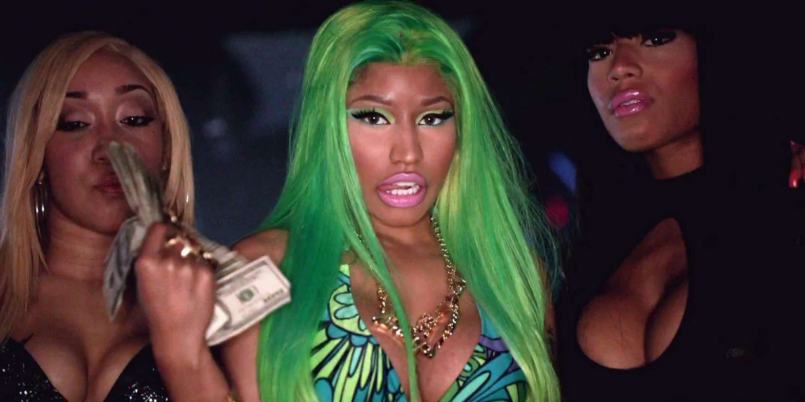 Nicki Minaj wearing a green wig and holding a stack of money surrounded by two girls