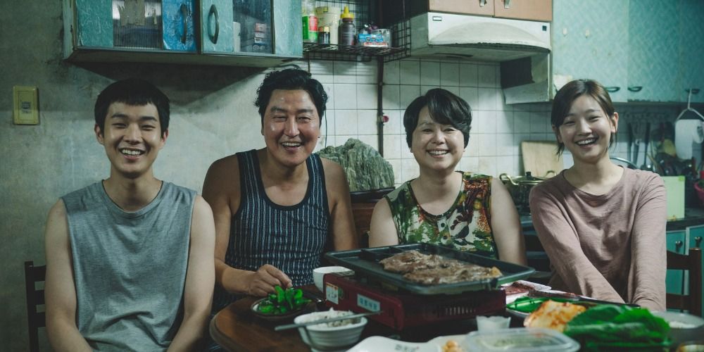 Ki Taek and his family smiling at the dinner table in a scene from Parasite