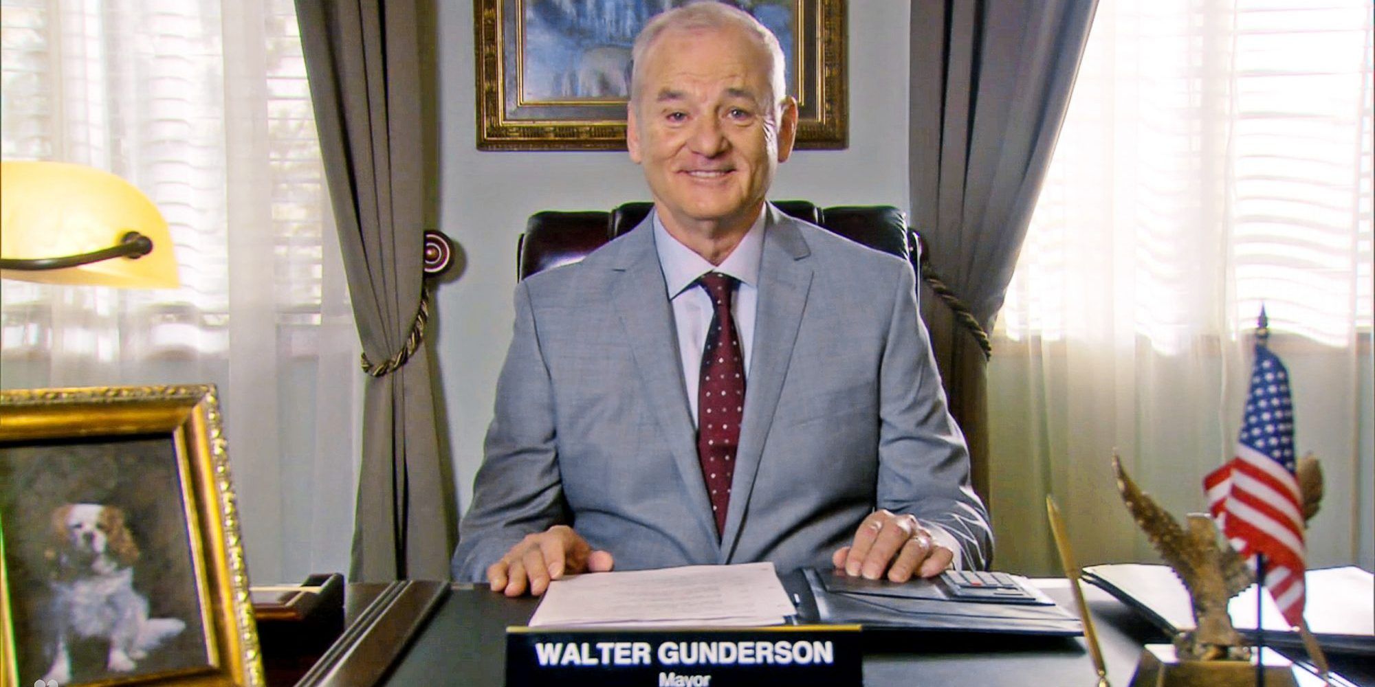 Bill Murray como prefeito Gunderson sentado na mesa em Parks and Rec