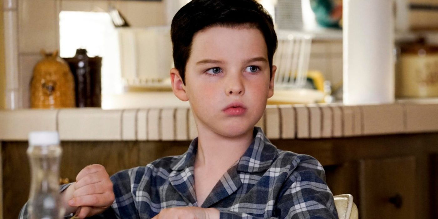 Sheldon in Young Sheldon sitting at the table, looking at someone or some thing.