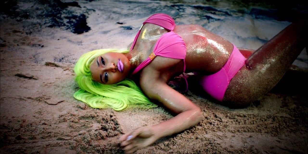 Nicki Minaj laying on a beach, wearing a green wig and pink bikini in the music video for &quot;Starships&quot;