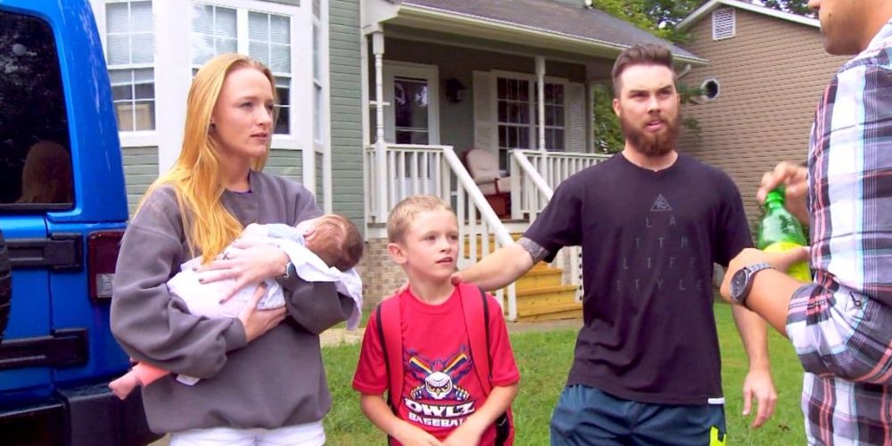 Maci holding her baby and standing outside with son Bentley and husband Taylor and talking to Ryan