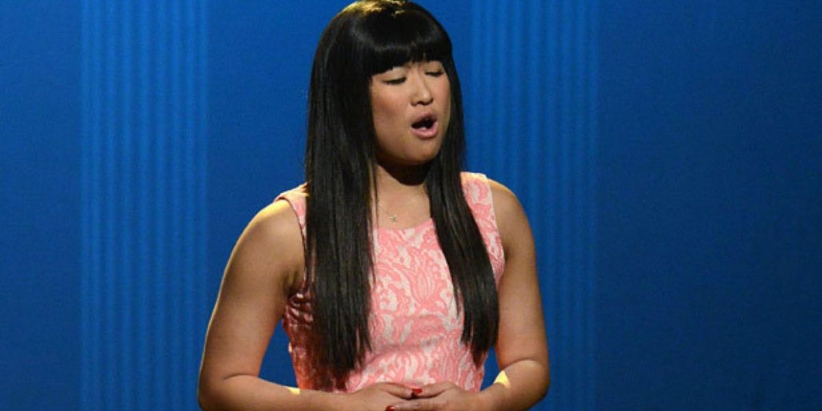 Tina wearing a pink dress and singing in the auditorium in Glee