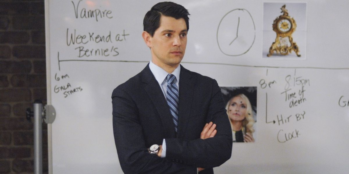 Josh Segal in a suit standing in front of a white board that has theories about the murder case they're workig on