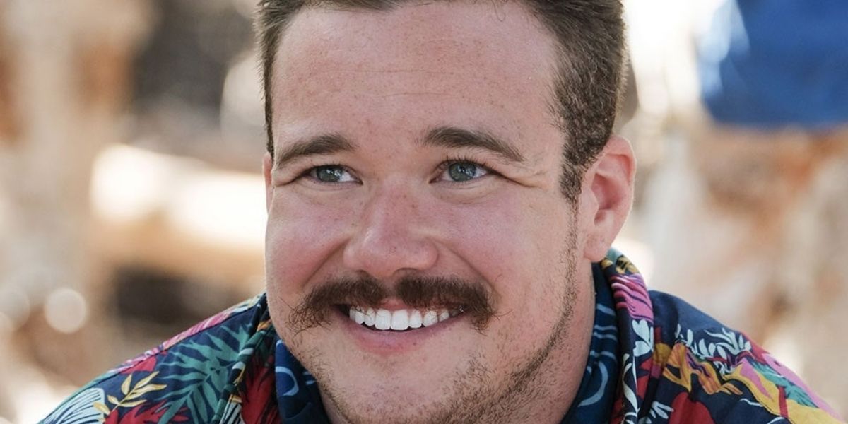 Zeke Smith sitting on the sand and smiling
