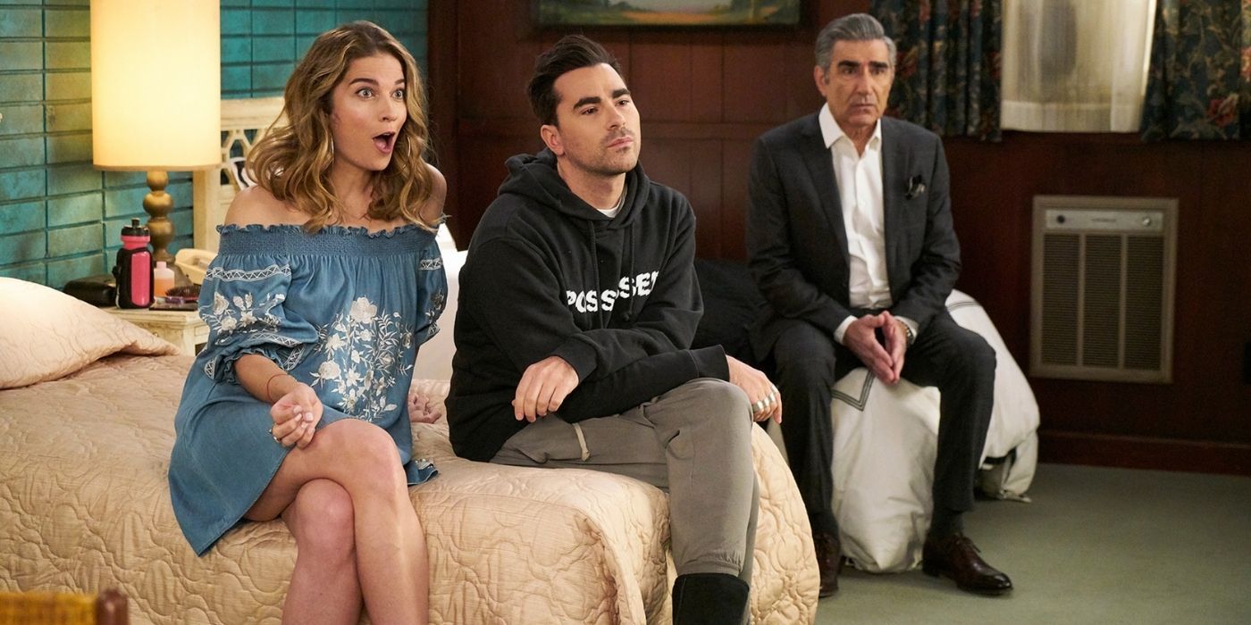 alexis, david, and johnny sitting on the beds at the motel in schitt's creek