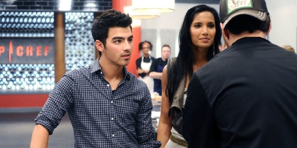 Joe Jonas in a blue shirt standing next to Padma Laxmi on Top Chef