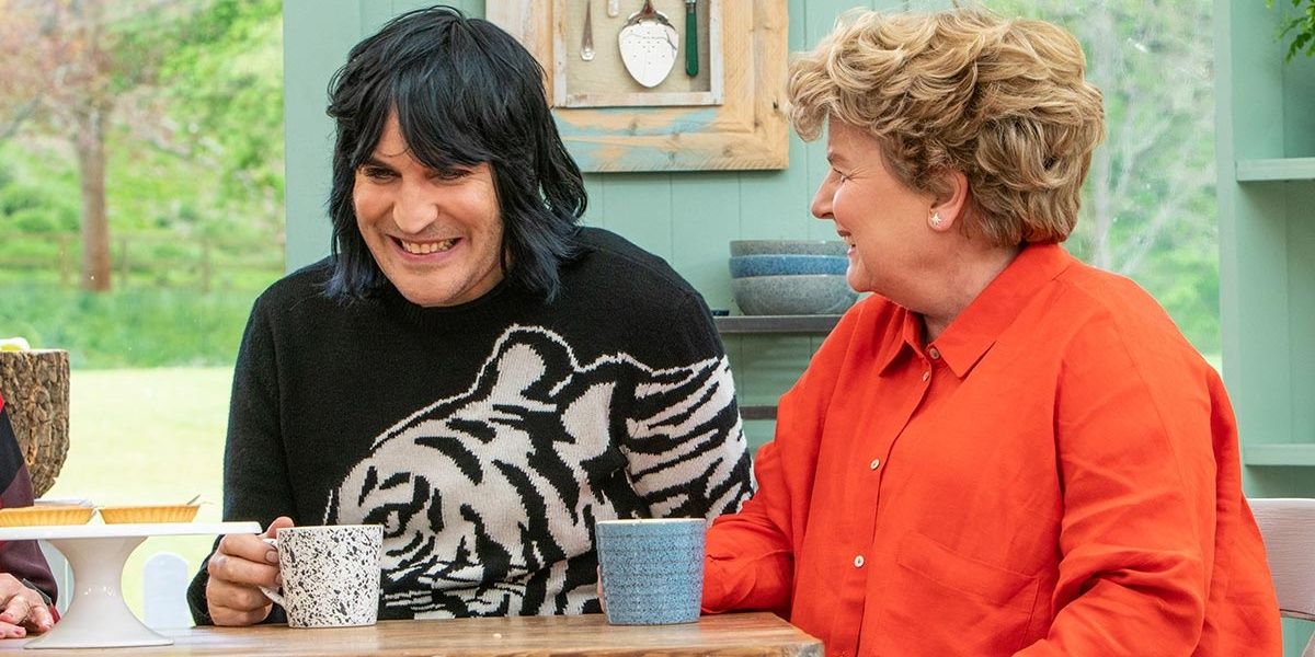 Noah Fielding in a black and white sweater with a cup around his hand sitting next to Sandi Toksvig