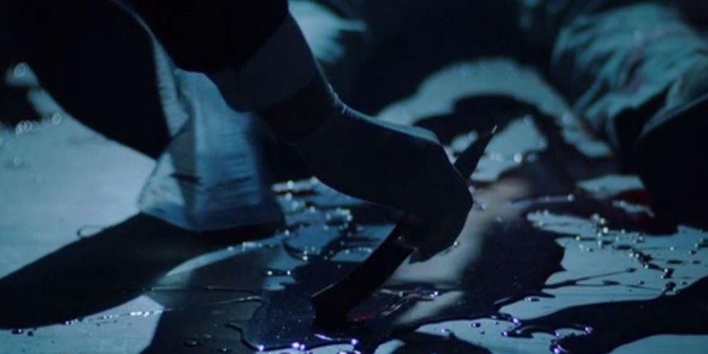 A man picks up a bloody knife from the ground next a body in The Conjuring The Devil Made Me Do It