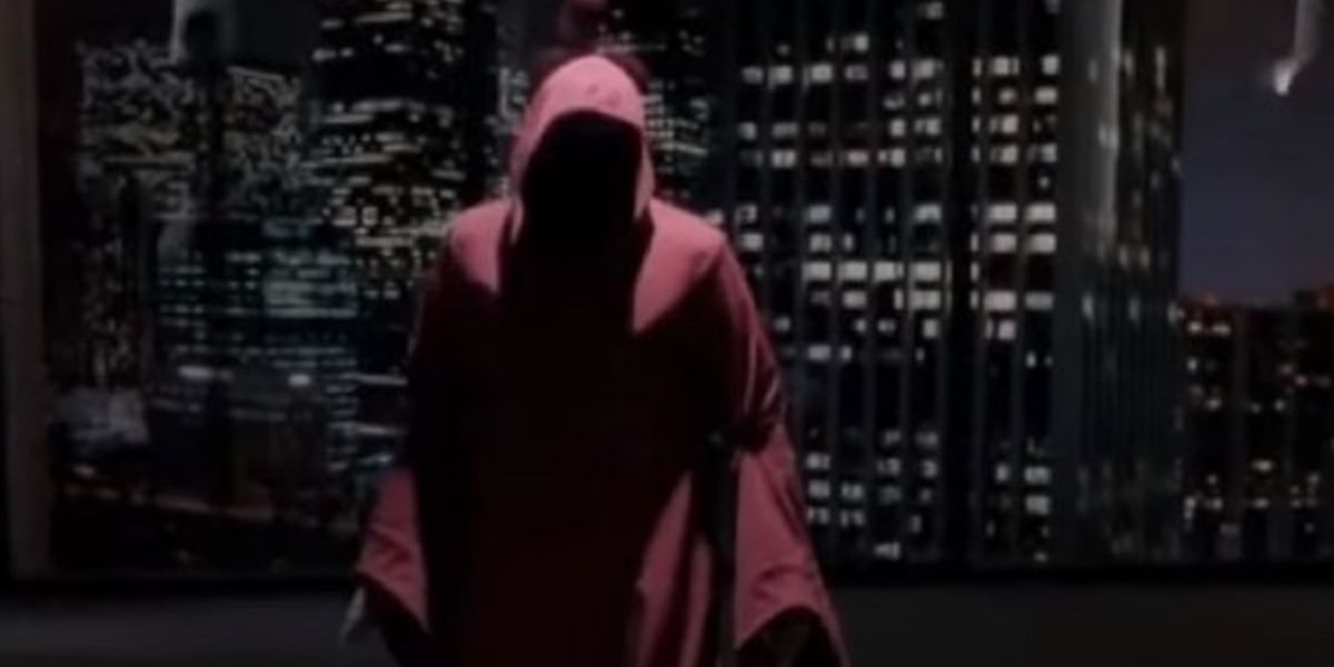 A hooded figure standing in front of a window