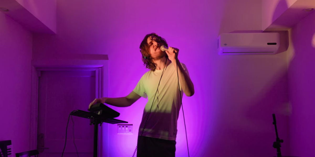 Bo Burnham with a microphone in an empty room with purple lights