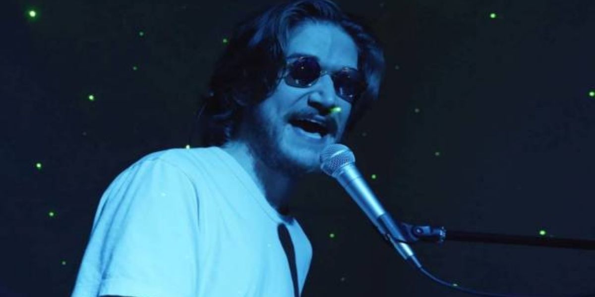 Bo Burnham wearing sunglasses in the dark and singing while playing the piano