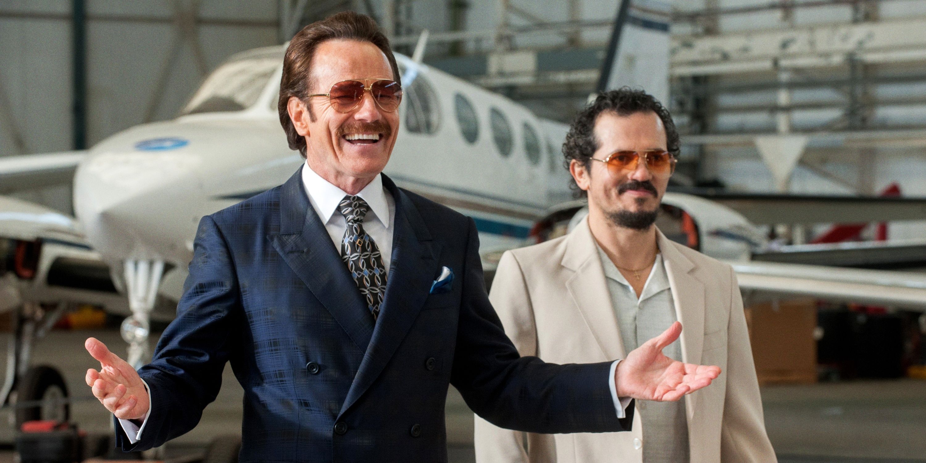 Bryan Cranston and John Leguizamo in The Infiltrator smiling and standing in front of a plane