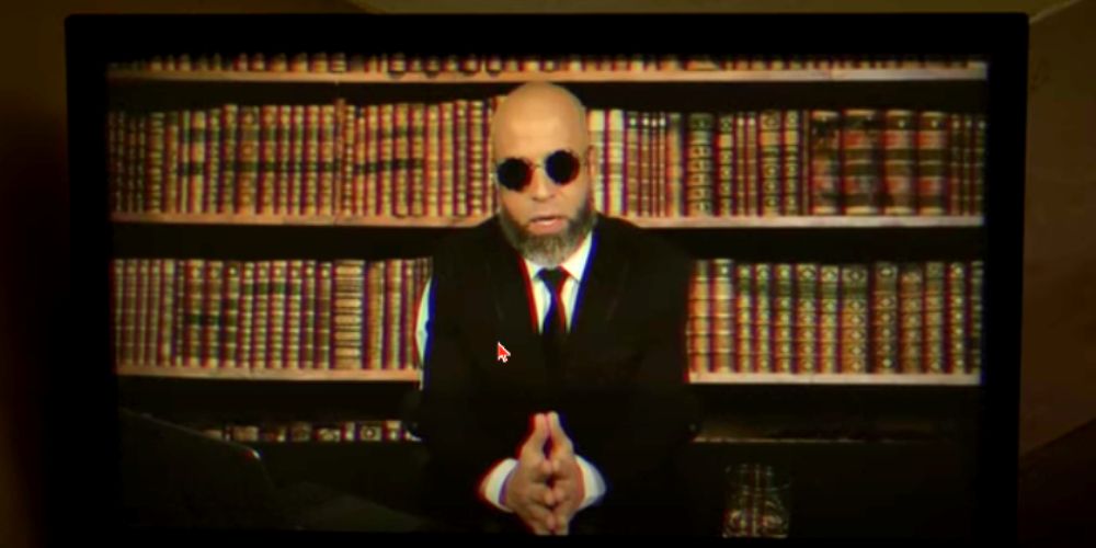 Chris Daughtry as Hugo Strange sitting in front of a bookshelf in Batman Dying Is Easy