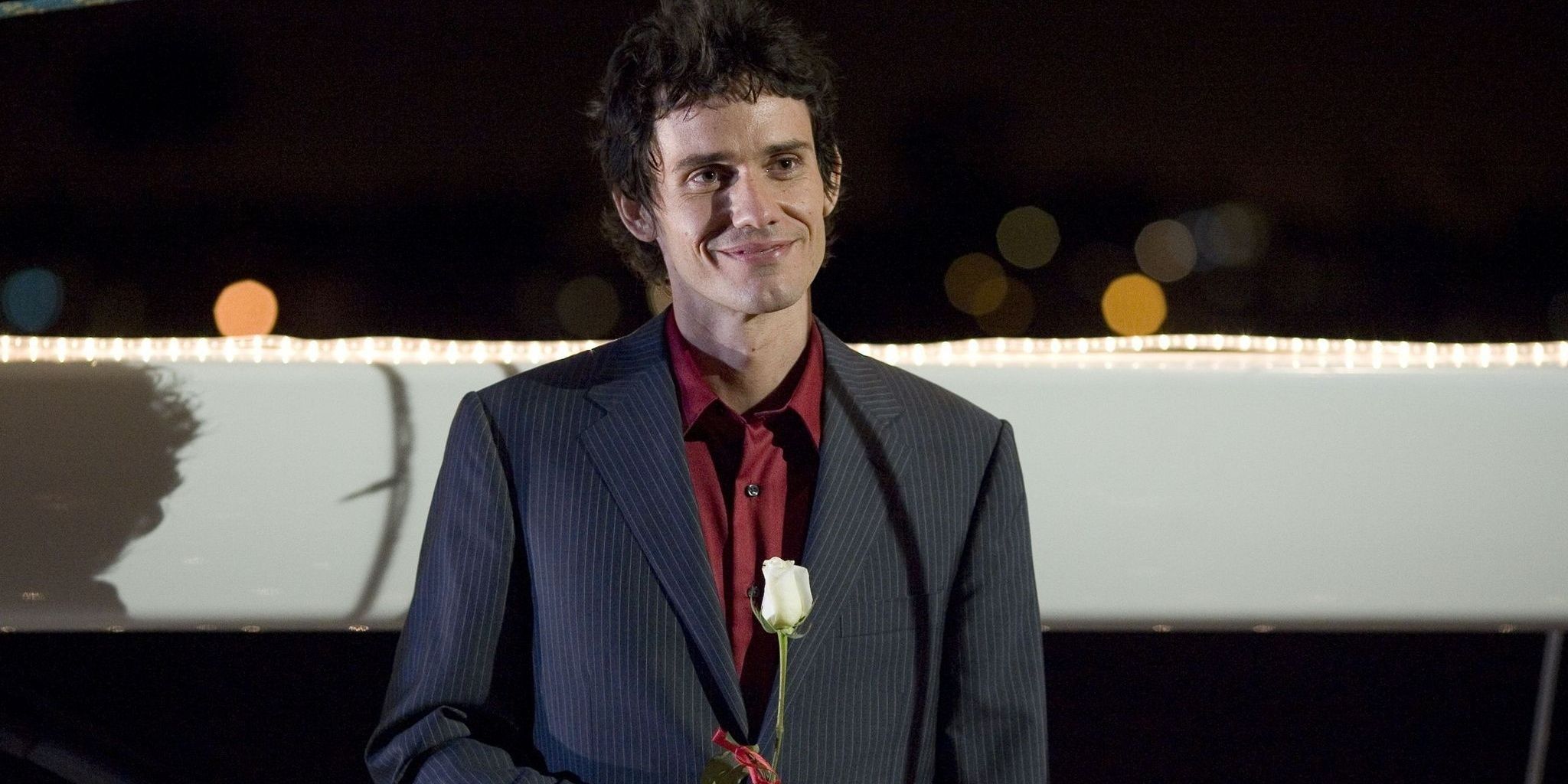 Christian Camargo as Rudy wearing a tuxedo and smiling