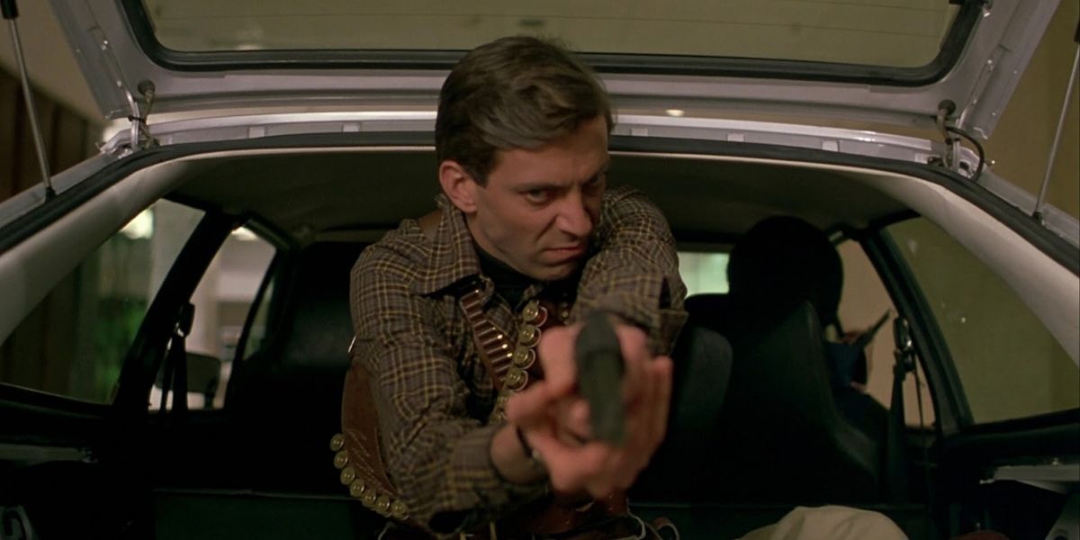 Male character in the trunk of a car points gun at the camera