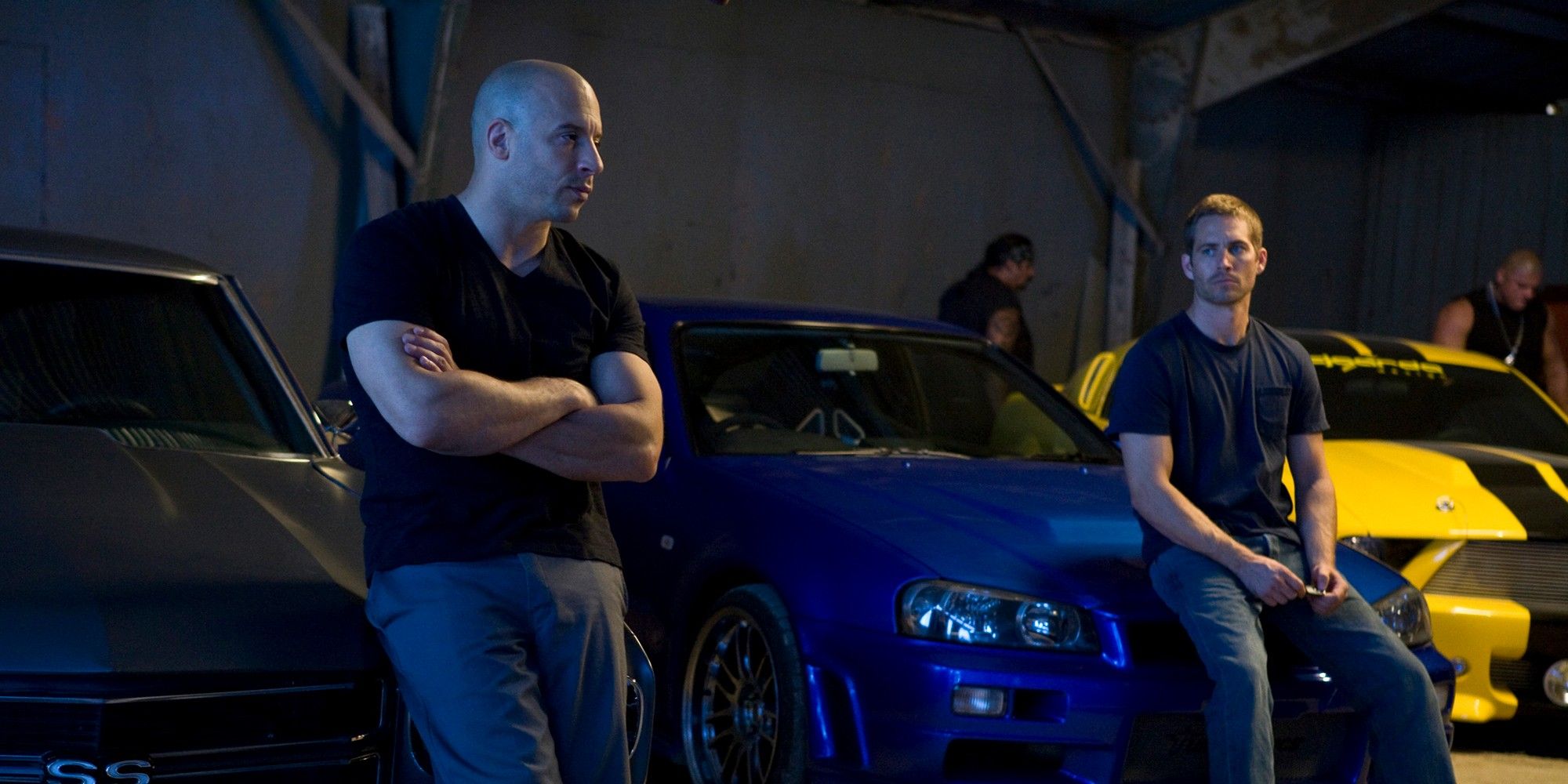 Brian and Dom sit on the hoods of their cars in a garage in Fast & Furious