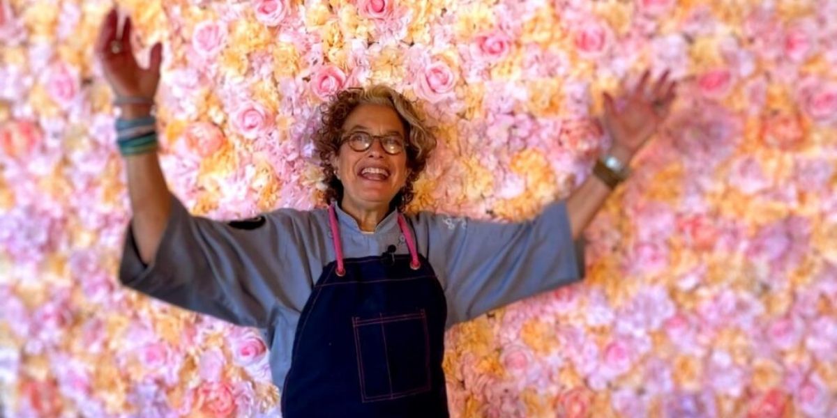 A woman standing in front of a flower-covered wall, raising her arms in celebration
