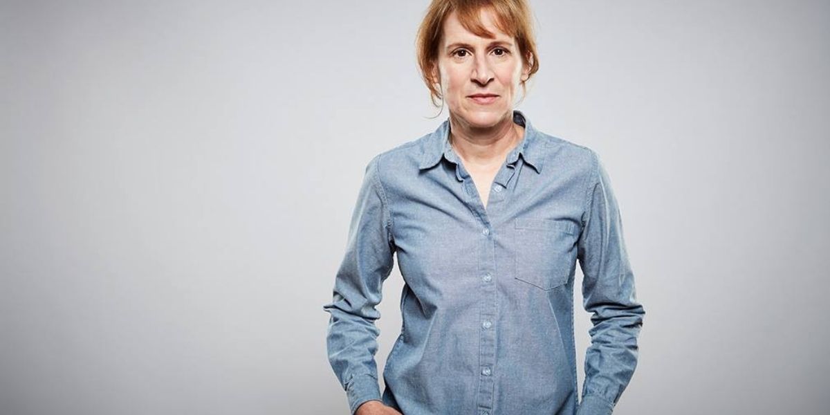 Kelly Reichardt with her hands inside her pockets standing against a grey background