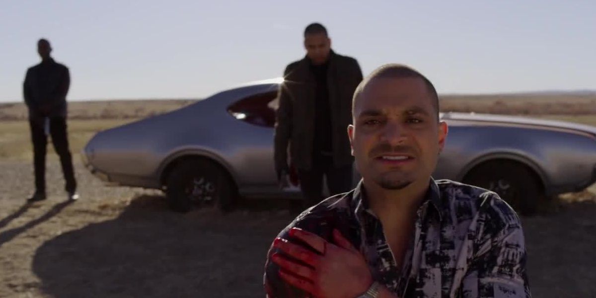 Nacho holding his bleeding arm in desert with Gus Fring's men behind him