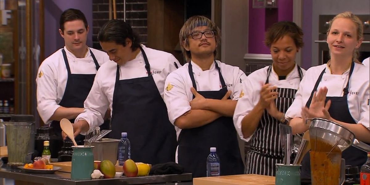 Five chefs listen to instructions while in a kitchen