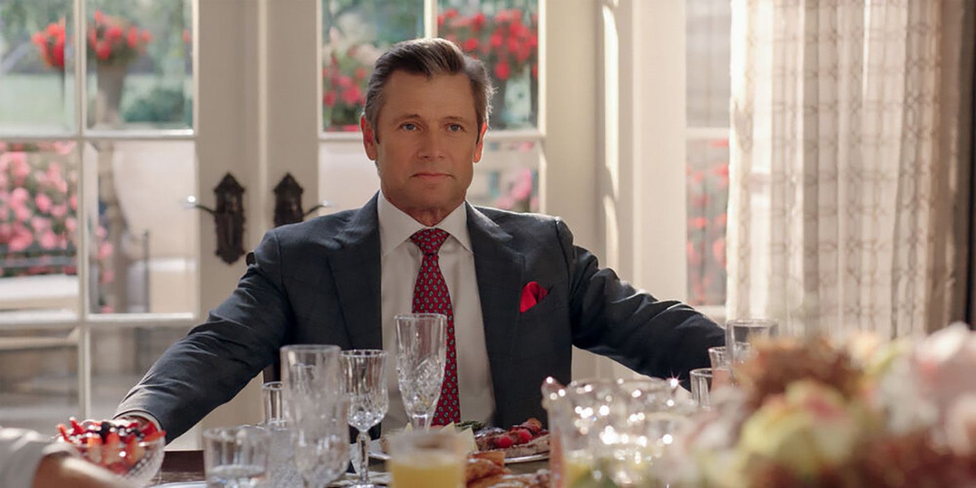 Blake Carrington from Dynasty sitting at the table, his arms outstretched