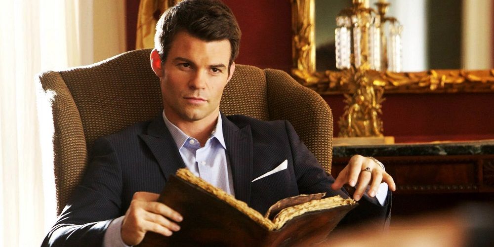 Elijah sitting down holding an open book in The Originals