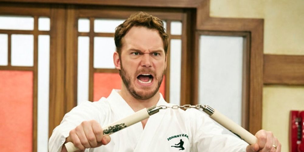 Andy from Parks and Recreation in a karate uniform, screaming, holding nunchucks