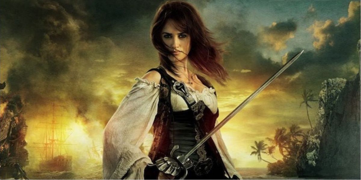Angela holds a sword before a sunset on a beach in Pirates Of The Caribbean