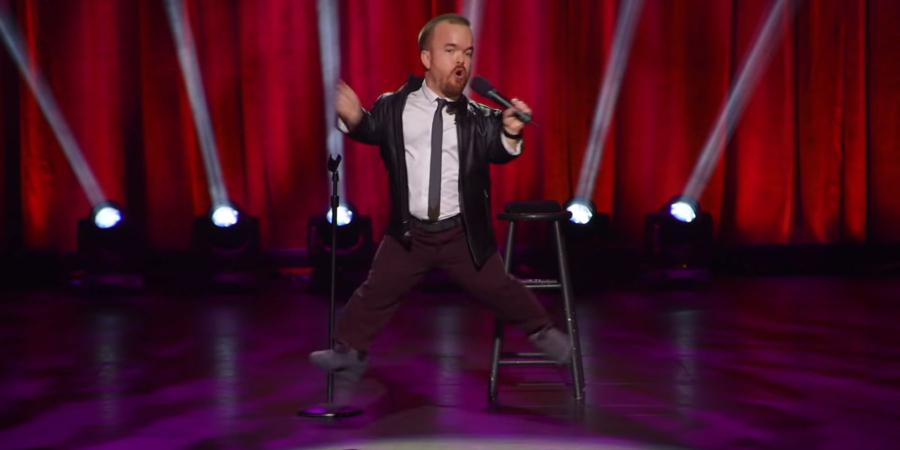 Brad Williams in Daddy Issues jumping into the air holding a mic.