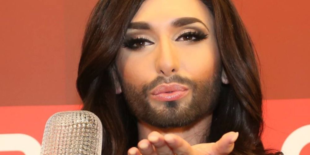 Conchita Wurst celebrating their Eurovision win, blowing a kiss to the camera and holding the trophy