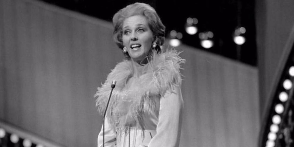 Katie Boyle hosting Eurovision wearing a white dress with a fur neckline