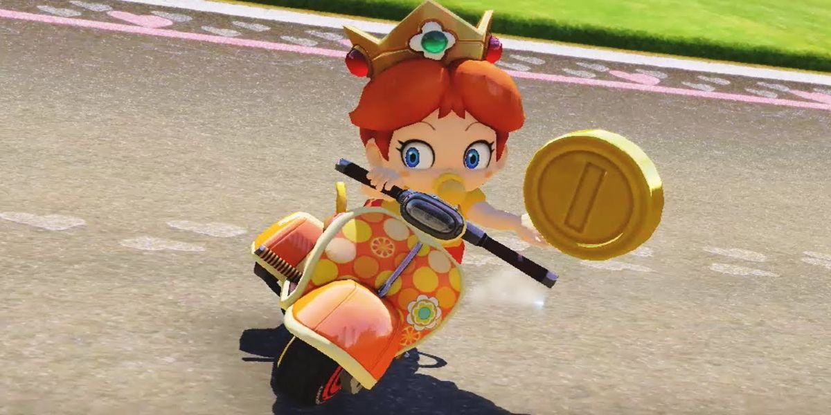 Baby Daisy dari Mario Kart 8 memegang koin emas di tangannya saat mengendarai skuter