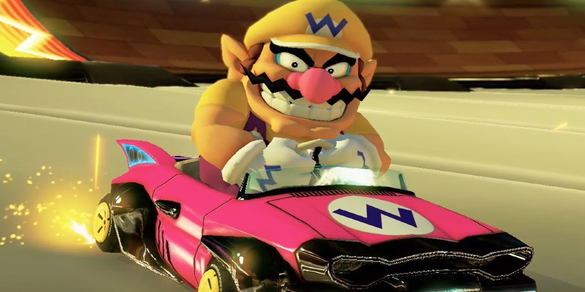 Wario mengendarai kart merah muda di Mario Kart 8, menyeringai ke arah kamera