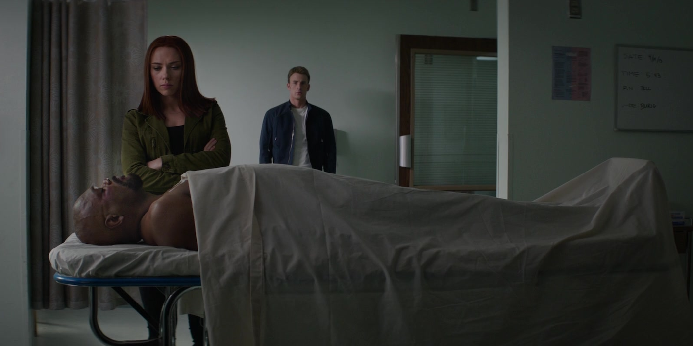 A man lies on a hospital gurney as a woman and another man look on