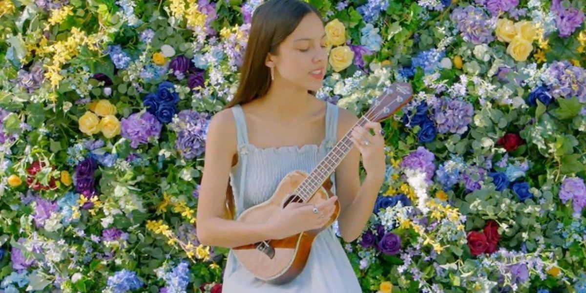 Olivia performing with her ukulele in front of a floral wall