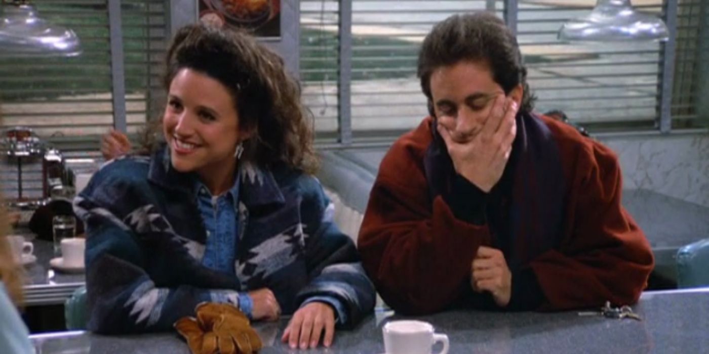Elaine smiles and Jerry covers his mouth while at a diner in Seinfeld