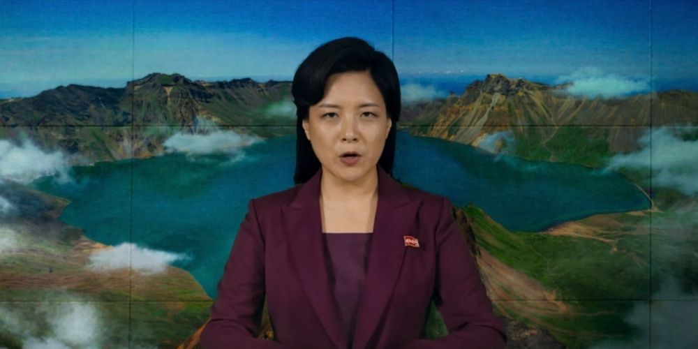 A news anchor introduces the news against the backdrop of mountains and water