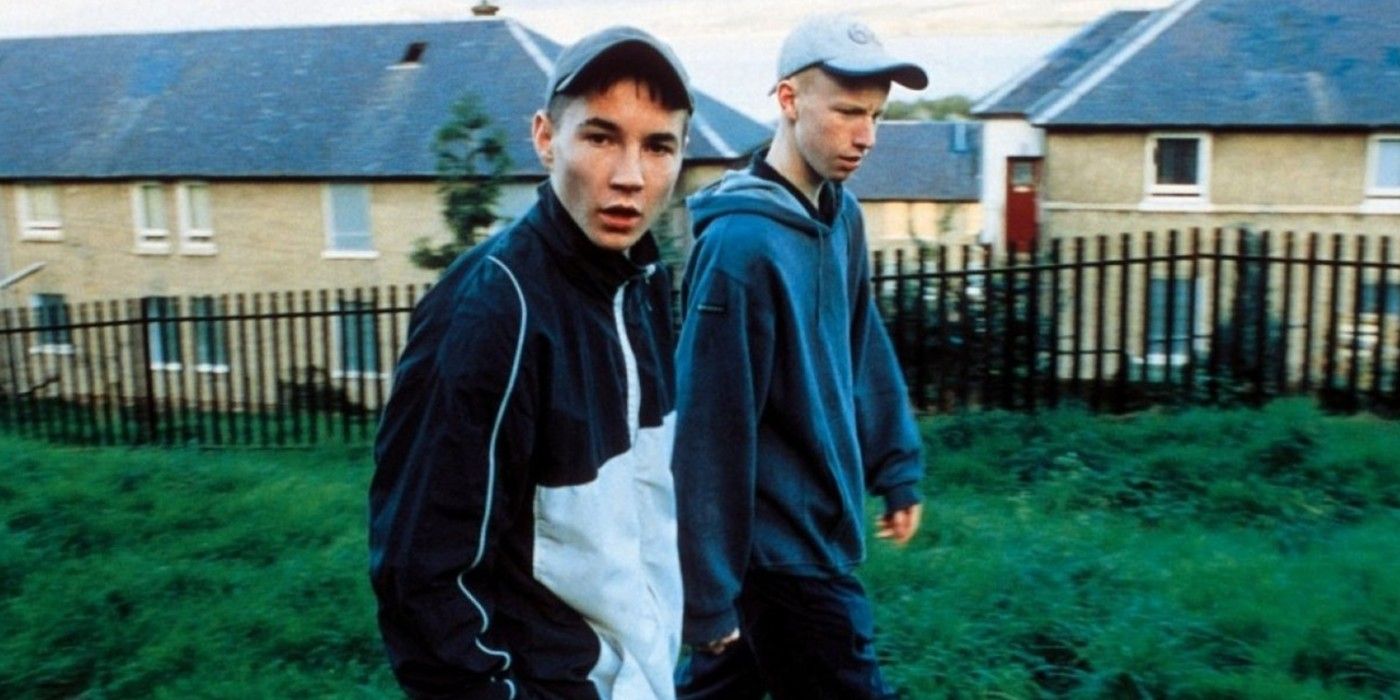 Two young men in hoodies and hats walk through a housing area in Sweet Sixteen