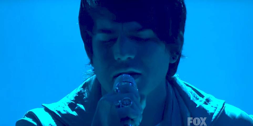 Adam Lambert chantant avec un fond sombre.