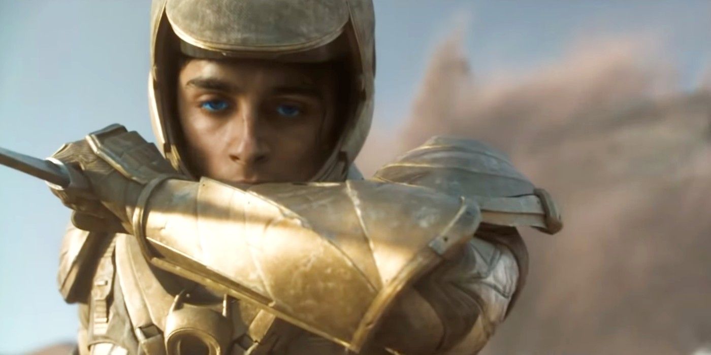 Paul's eyes glow blue as he wears a golden armor and the sand scatters behind him in Dune (2021).