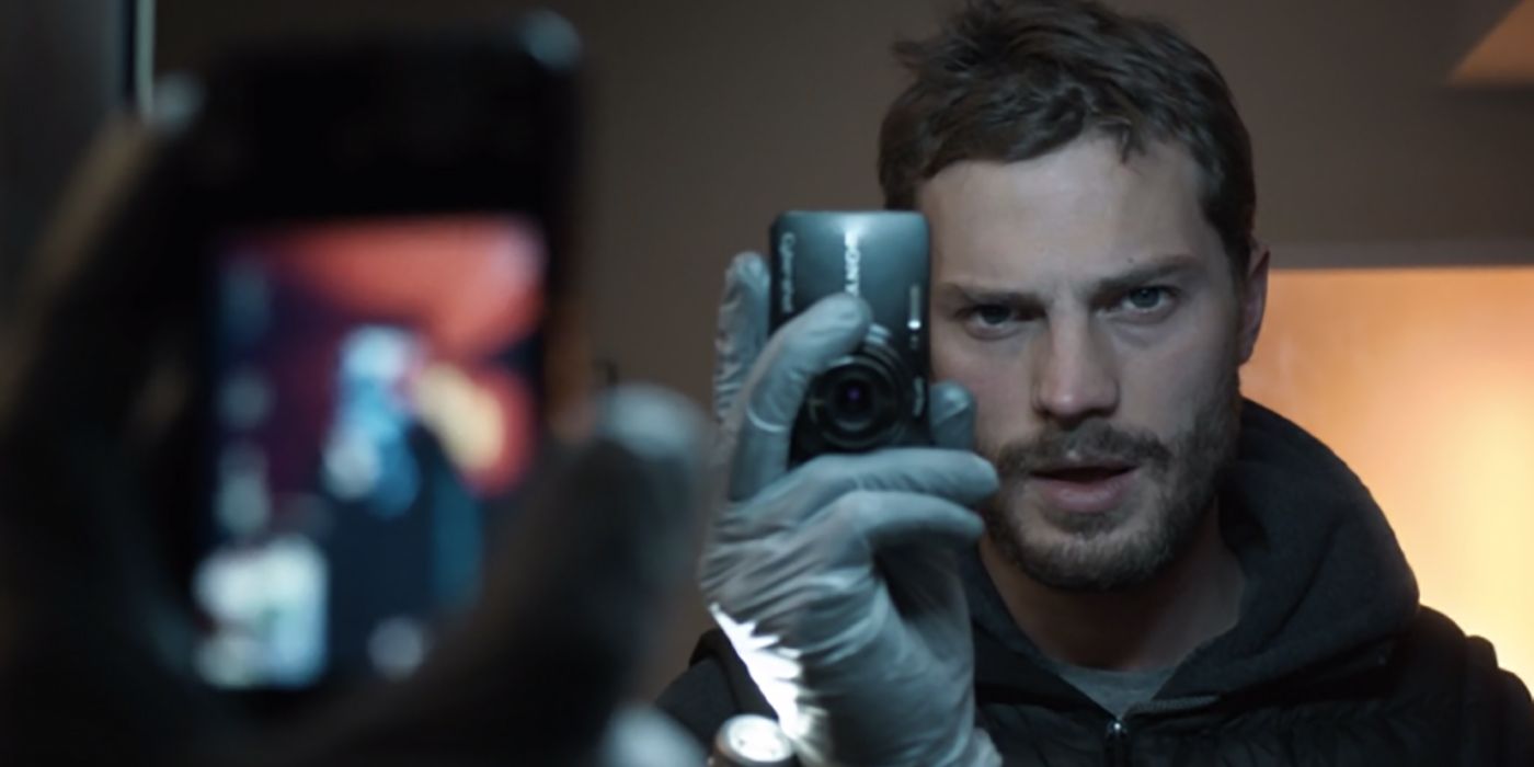 Jamie Dornan holding a camera up to a mirror, looking at himself.