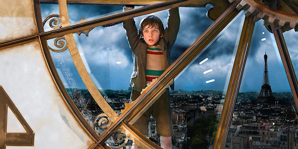 Hugo hangs onto a giant clock hand with the Eiffel Tower in the background in Hugo