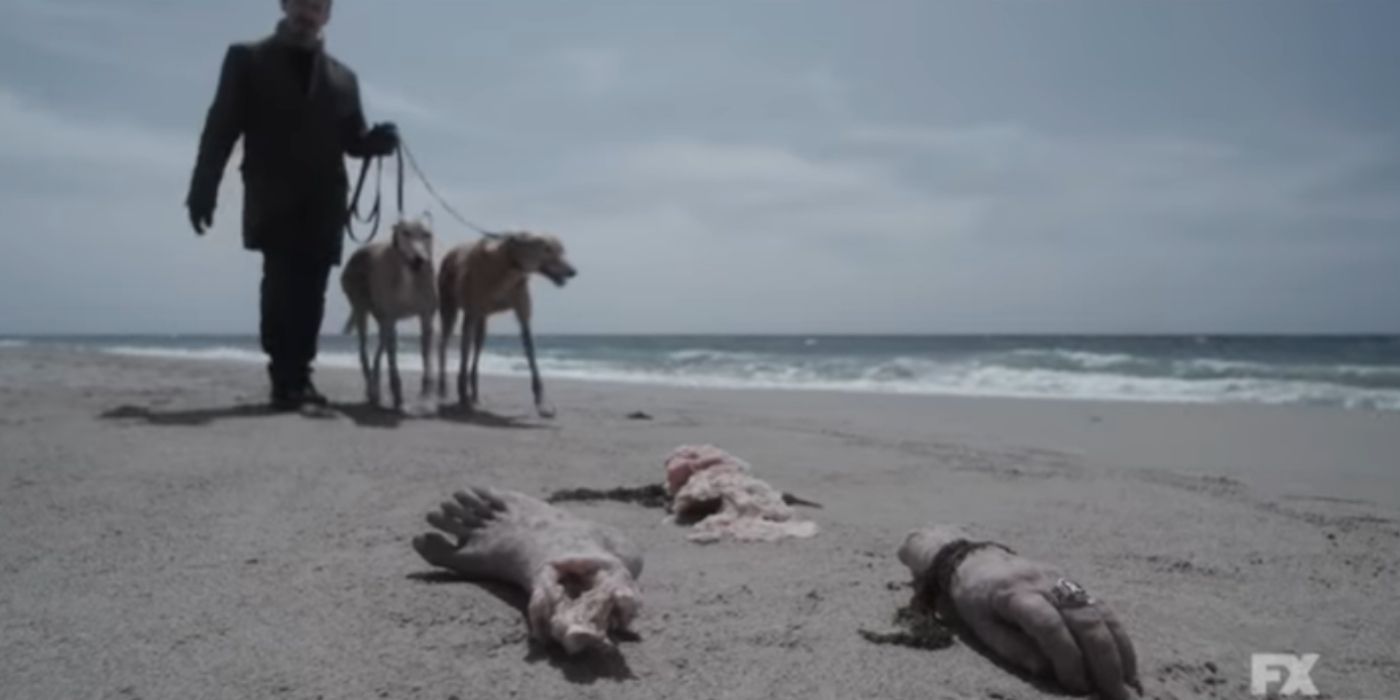 A man walk his dogs on a beach with limbs on the sand in American Horror Story: Double Feature