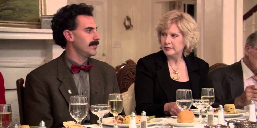 Borat sits in the middle of two women at a dinner party in Borat