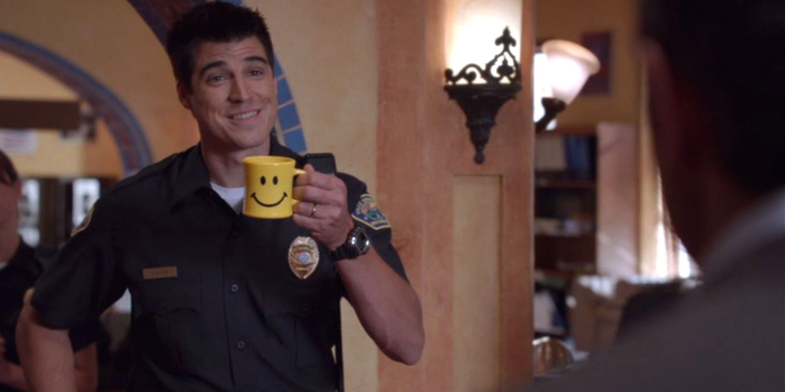 Buzz McNab holding a smiley face mug at the precinct in Psych